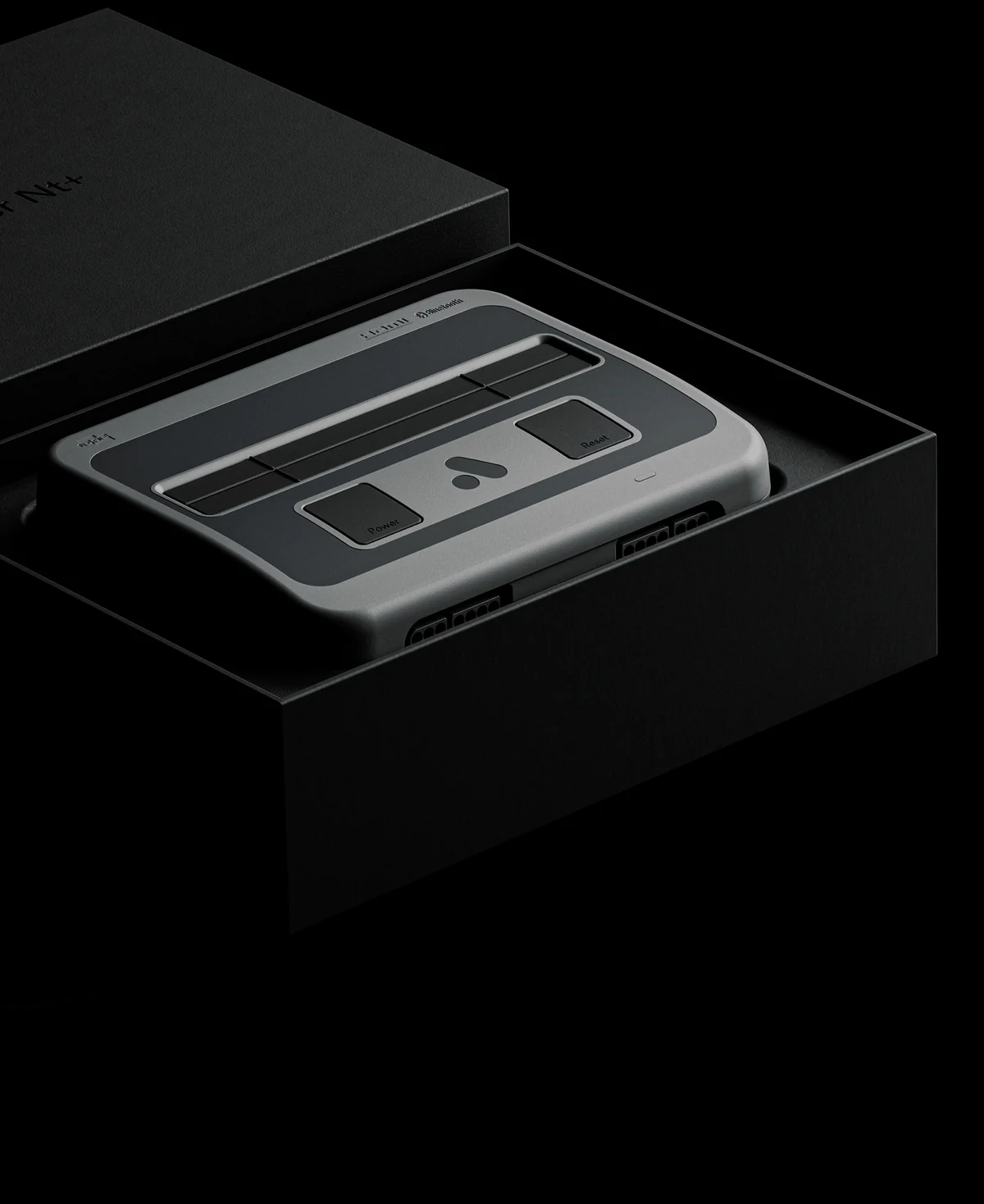 Une console Super Nt+ grise dans sa boîte noire ouverte, le couvercle posé derrière