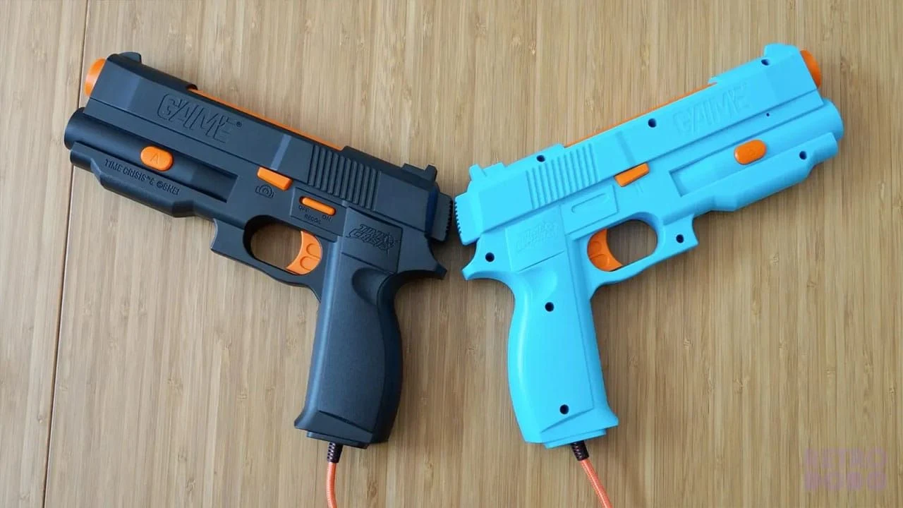Photo de deux pistolets optiques G'AIM'E posés sur une surface en bois, l'un noir avec inscription « G'AIM'E » moulée dans le boîtier et boutons orange, l'autre bleu clair, reliés chacun à un câble à gaine orange