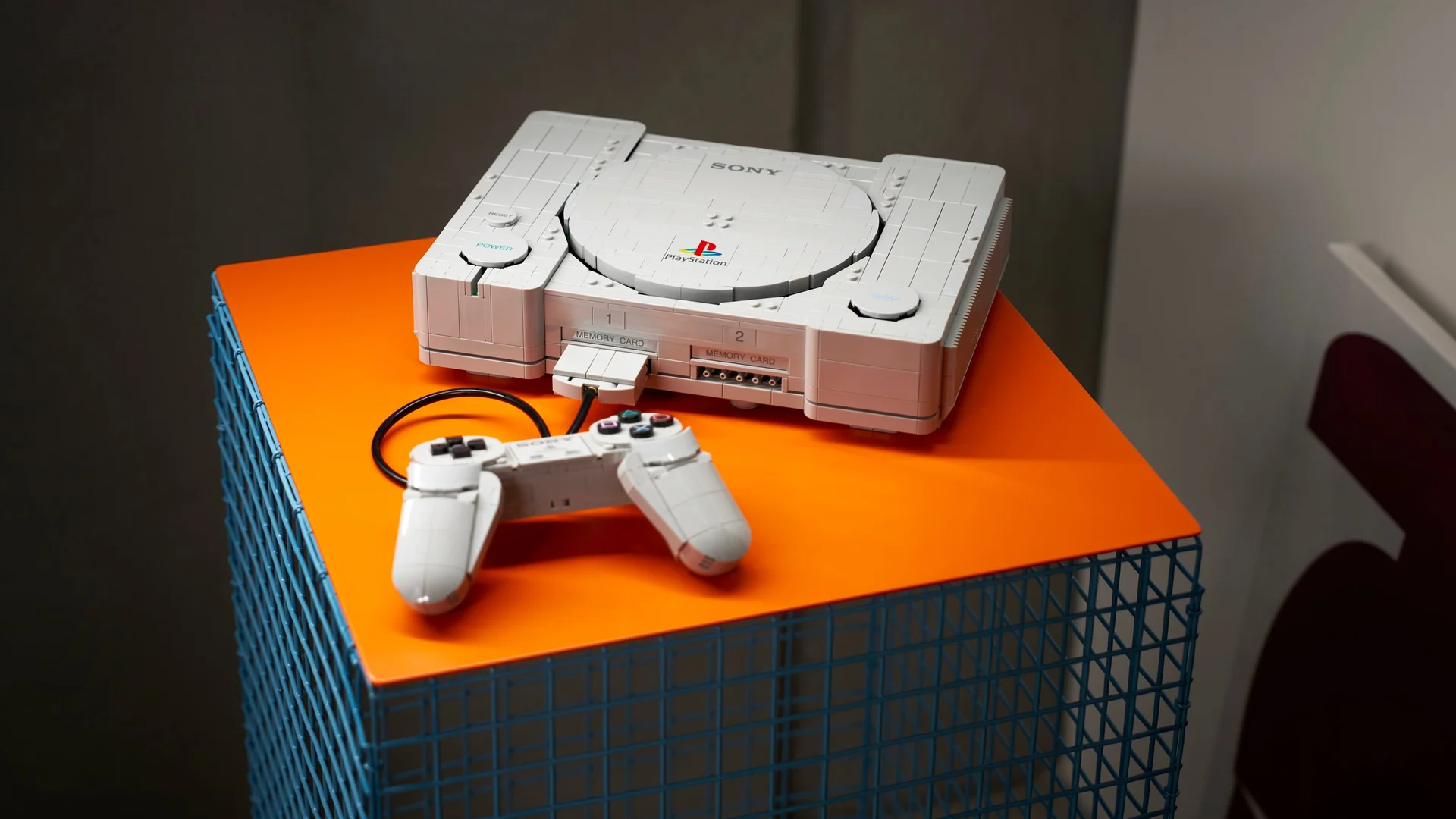 Le set LEGO PlayStation monté et posé sur un socle orange, sa manette branchée devant lui