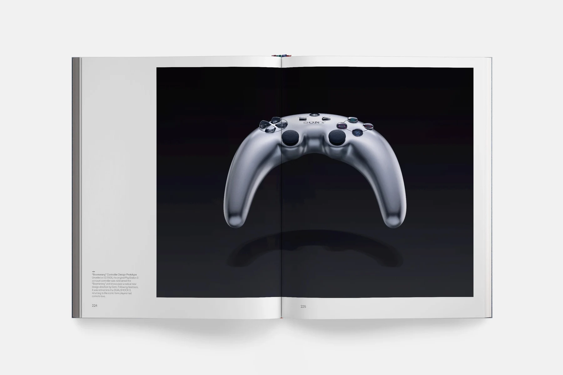 Double page du livre : une manette grise en forme de boomerang photographiée sur fond noir