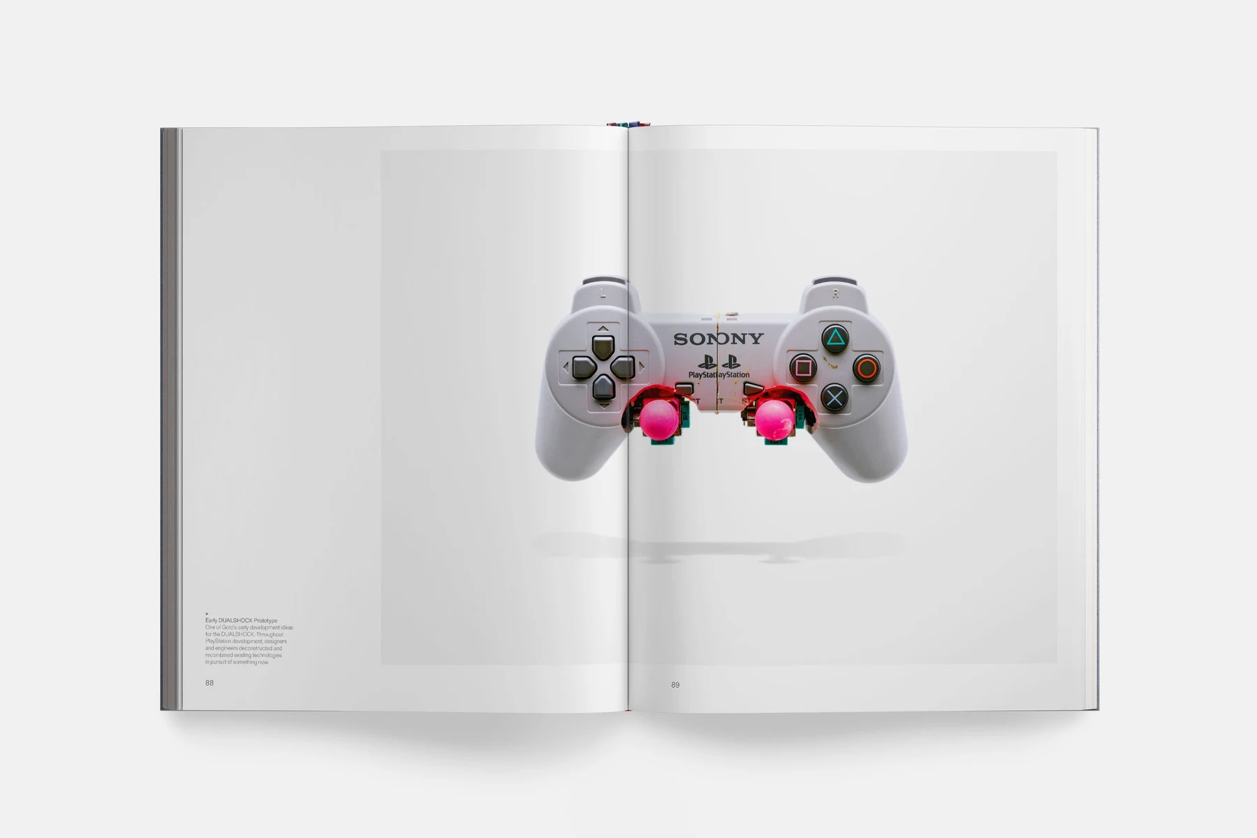 Double page du livre : un prototype de manette grise aux deux sticks roses, sur fond blanc