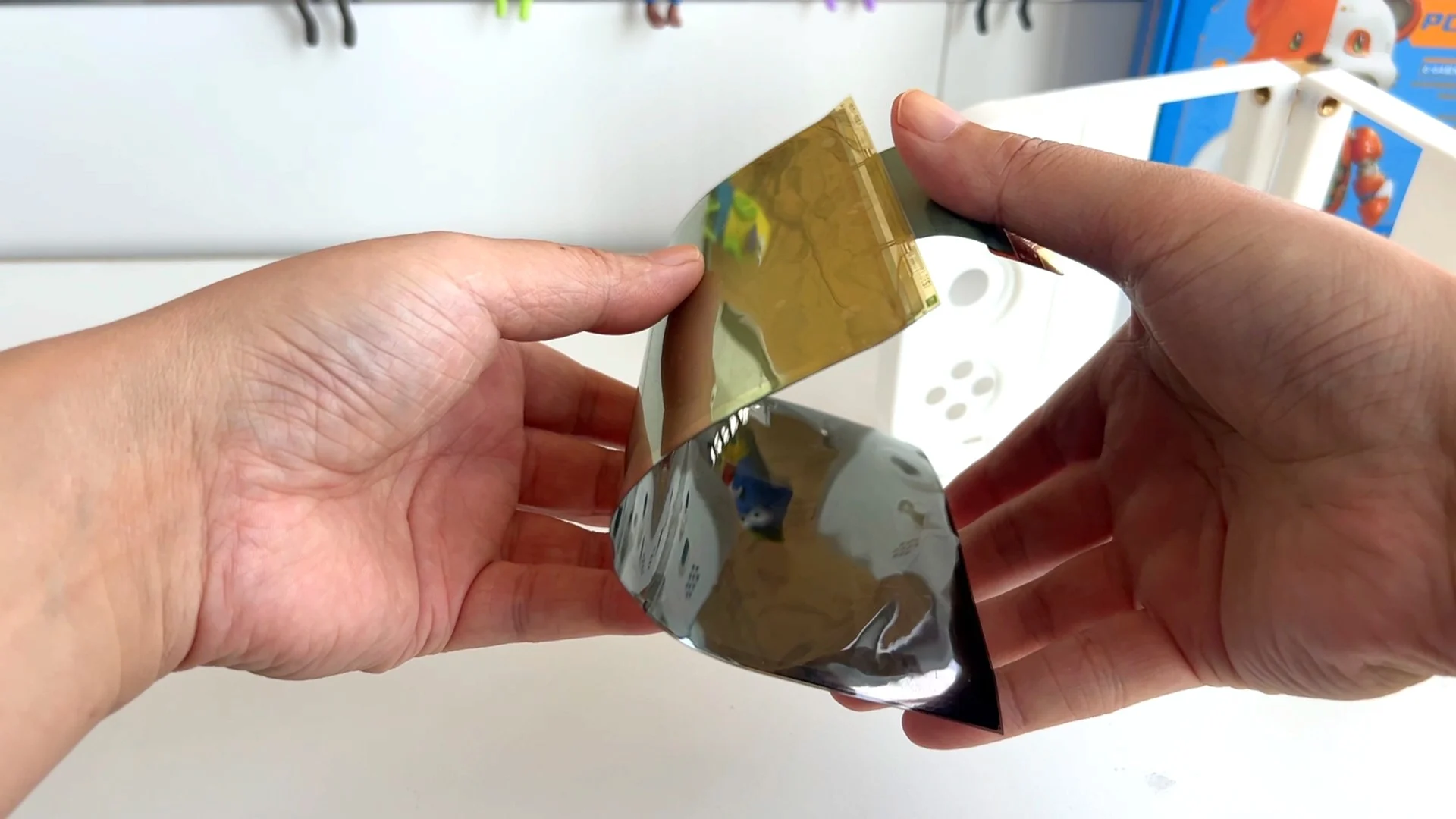 Deux mains tiennent un écran souple nu, courbé, avec sa nappe de connexion dorée