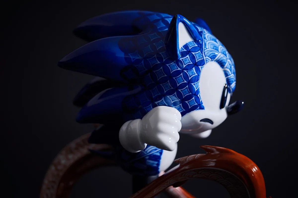 La statue vue de trois quarts : la tête et le torse de Sonic couverts de motifs bleus de cercles et de vagues, un poing serré et le haut de la boucle rouge