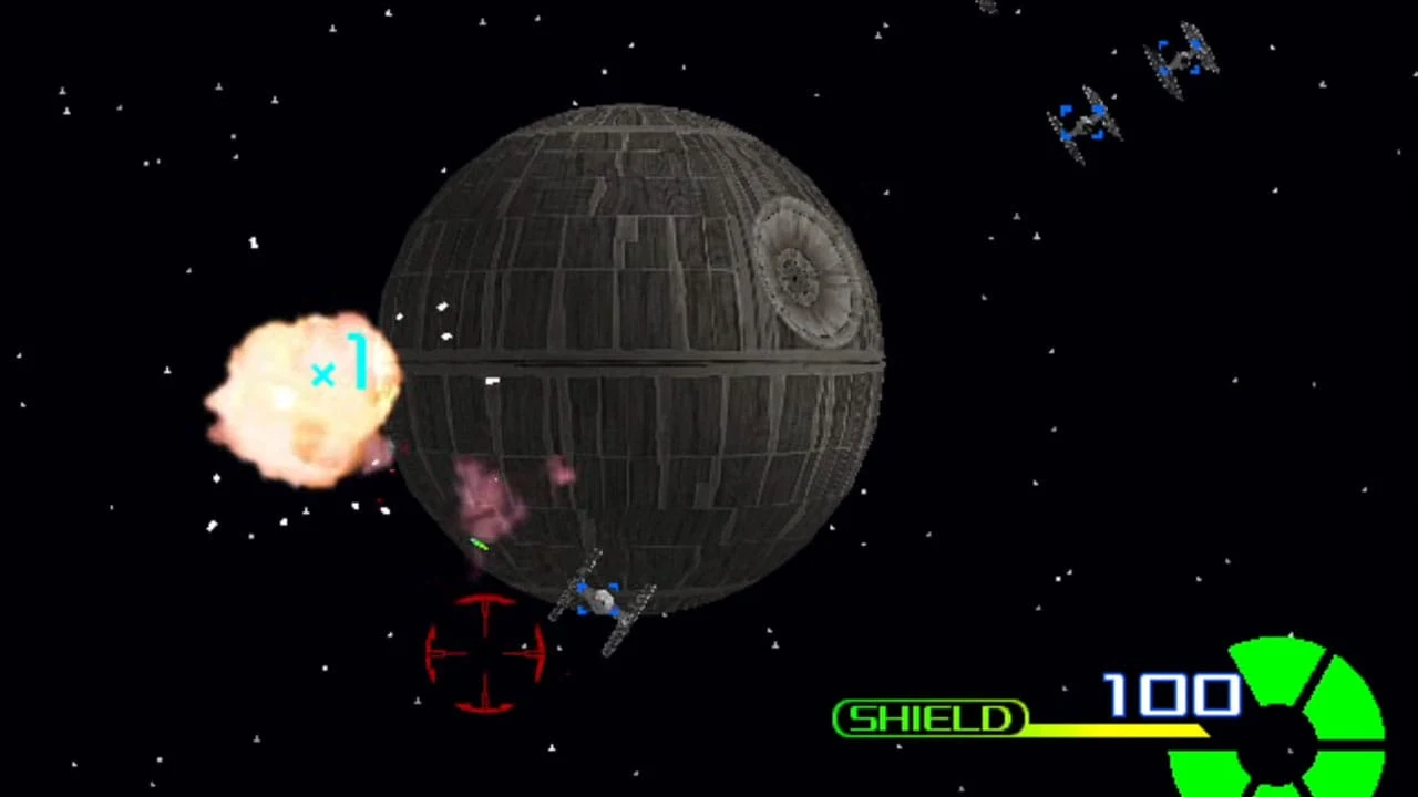Capture d'écran du portage Dreamcast de Star Wars Trilogy Arcade : vue à la première personne d'un chasseur visant l'Étoile noire dans l'espace, une explosion orangée sur la gauche, des chasseurs TIE au loin et au premier plan, avec une jauge de bouclier « SHIELD 100 » en bas de l'écran