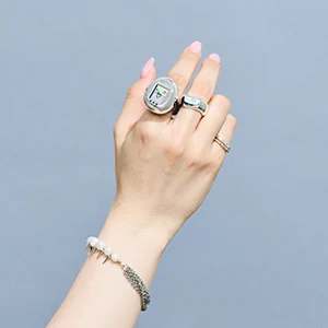 Le Tamagotchi ring porté au doigt, à côté d'autres bagues : les commandes se trouvent sur les côtés du boîtier, les trois boutons de façade n'étant que décoratifs.