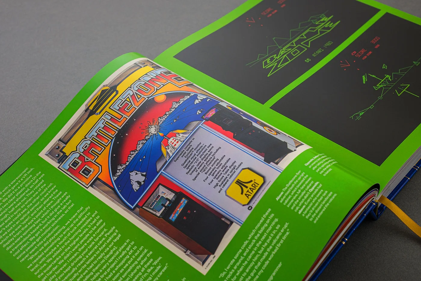 Double page du livre sur fond vert : prospectus de la borne Battlezone d'Atari et deux captures du jeu en graphismes vectoriels