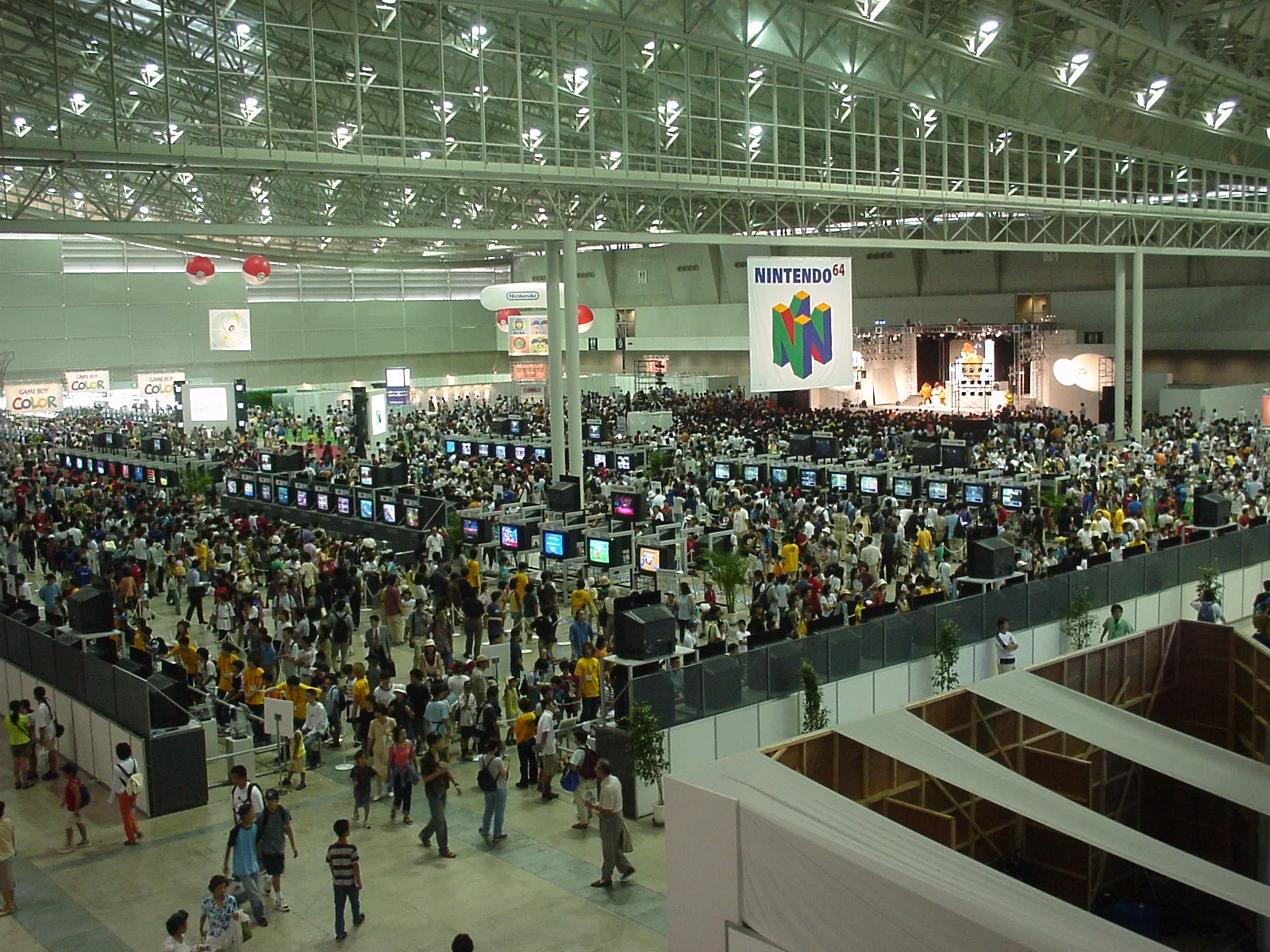 Vue plongeante sur un immense hall de salon rempli de visiteurs et de rangées de bornes de démonstration, avec une bannière Nintendo 64 suspendue au plafond