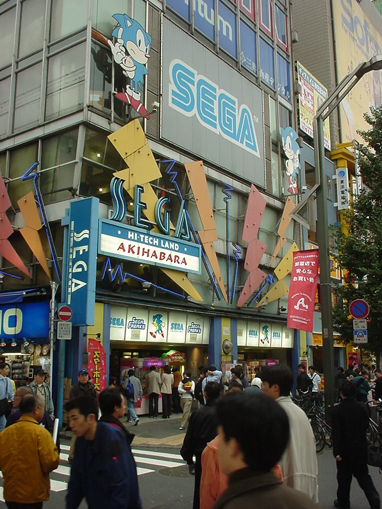La façade d'un immeuble de plusieurs étages aux couleurs de Sega, couverte d'images de Sonic, avec l'enseigne Hi-Tech Land Akihabara, au-dessus d'une rue animée