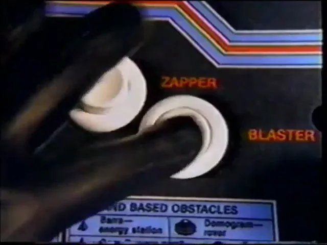 Image de la publicité : le tableau de commandes de la borne, avec un manche noir et deux boutons marqués ZAPPER et BLASTER